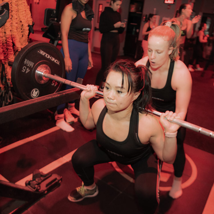 Athlete performing a back squat with a spotter behind them.